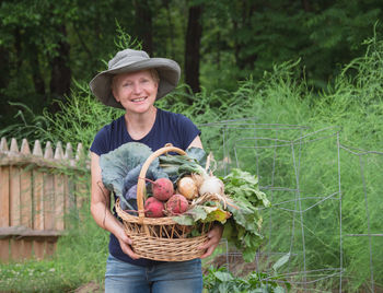 Portrait of smiling young woman holding basket in farm