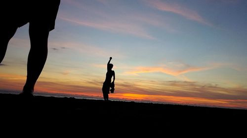 Silhouette man with arms raised against sky during sunset