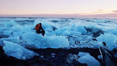 Man standing on snow covered sea during sunset