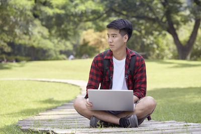 Young man looking away while sitting on mobile phone