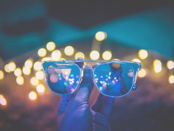 Cropped hand of woman holding sunglasses against illuminated lights