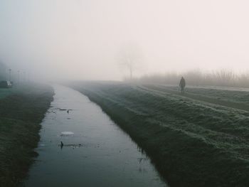 Rear view of man walking on road against clear sky in fog