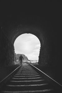 Man walking on railroad track in tunnel