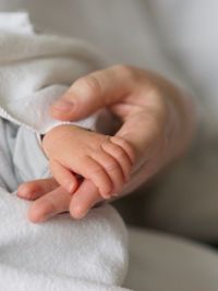 Close-up of mother and baby holding hands on bed