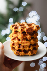 Homemade pumpkin and carrot waffles on a white plate against the background of a bright garland.