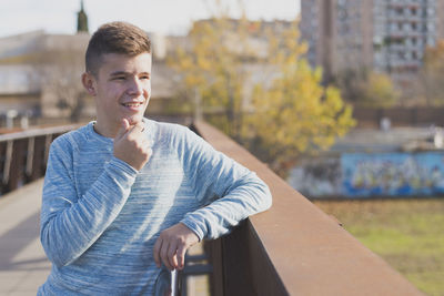 Thoughtful teenage boy standing on footbridge in city