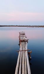 Wooden post in lake against sky during sunset