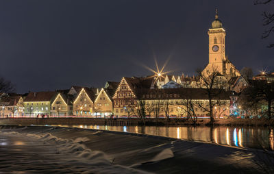 Illuminated buildings by river against sky at night