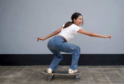 Full length of young woman skateboarding against wall