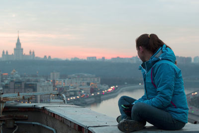 Man sitting in city against sky during sunset