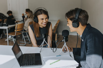 Smiling female and male students looking at each other during podcasting in classroom