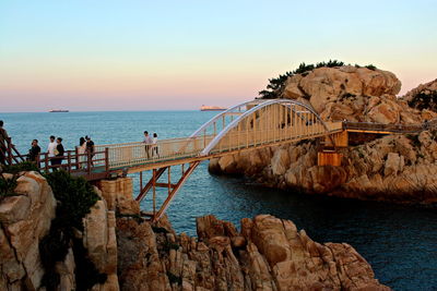 People walking on footbridge over sea against sky