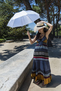 Woman holding umbrella while standing by tree