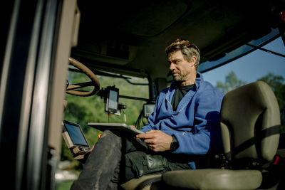 Mature farmer using tablet pc sitting in tractor on sunny day