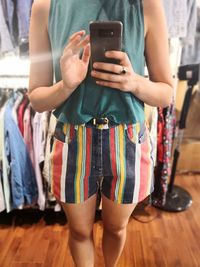 Midsection of woman photographing through smart phone in clothing store