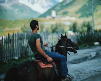 Side view of man riding horse against mountains