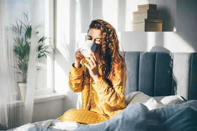 Young woman using mobile phone while sitting on bed at home