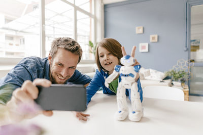 Happy father and son taking a selfie with robot on table at home