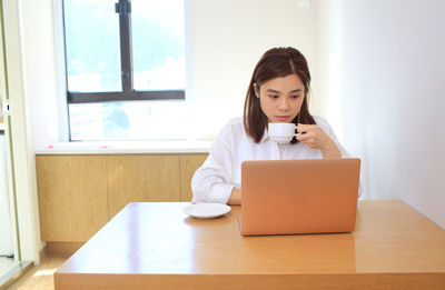 Young woman using mobile phone while sitting on table