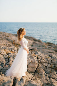 Woman on rock at beach against sky