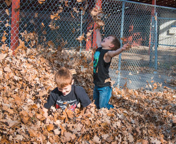 Siblings playing in leaves at park during autumn