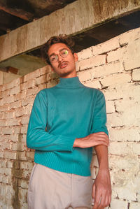 Portrait of young man standing by brick wall