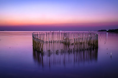 Wooden posts in sea against romantic sky at sunset