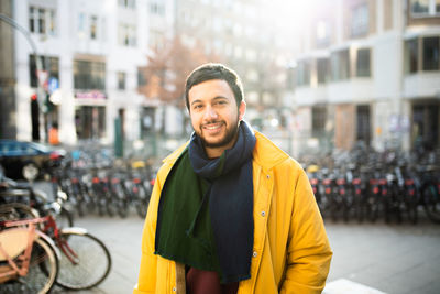 Portrait of smiling young man standing on footpath in city