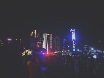 People at illuminated city against clear sky at night
