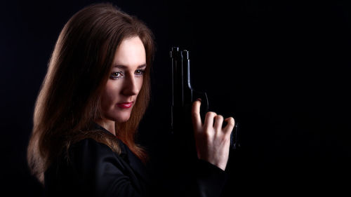 Woman looking away while holding gun against black background