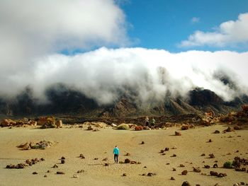 Man walking on field by cloud covered mountains against sky