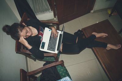 High angle view of young woman with laptop sitting on chair at home