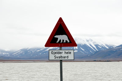 Road sign on snow covered landscape against sky