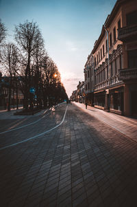 Empty road amidst buildings against sky during sunset