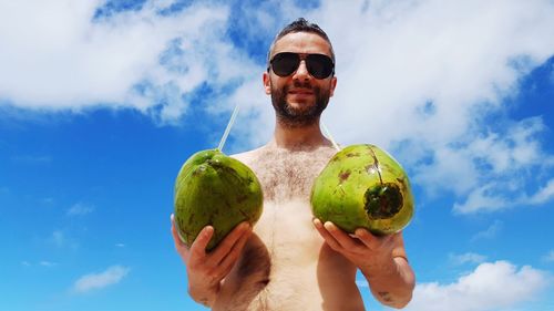 Portrait of man holding sunglasses against sky