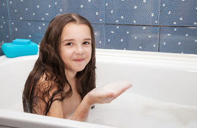 Portrait of smiling girl holding soap sud in bathtub