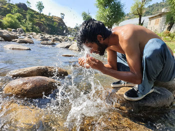 Side view of shirtless man splashing water in rriver 