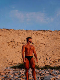 Shirtless man standing against brick wall