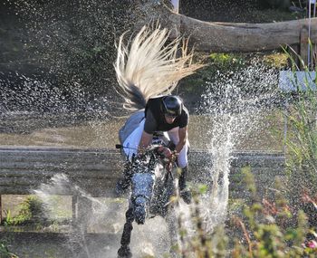 Jockey with horse jumping in puddle