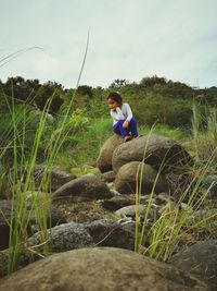 Full length of girl sitting on rock against sky