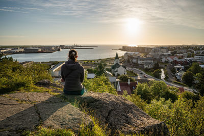 Rear view of woman looking at cityscape against sky during sunset