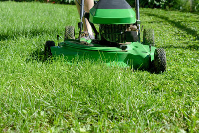 Low section of person with lawn mower on grassy field during sunny day