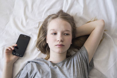 High angle view of girl holding mobile phone while lying down on bed