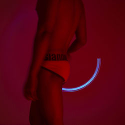 Midsection of man wearing underwear spinning lighting equipment against wall