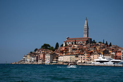 Buildings by sea against clear blue sky