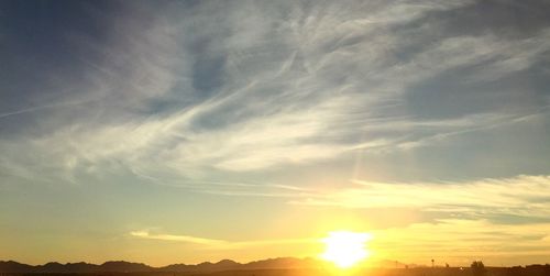 Low angle view of sunlight streaming through clouds during sunset