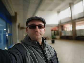 Portrait of young man wearing sunglasses standing against ceiling