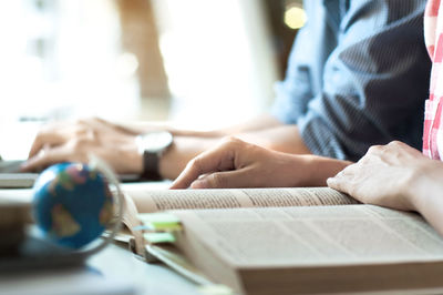 Midsection of woman reading book with male colleague at desk in office