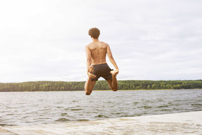 Full length rear view of man holding legs while jumping into lake