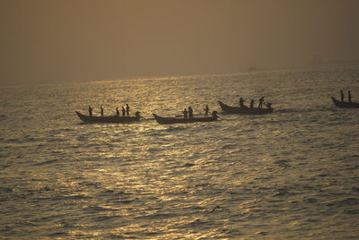 Silhouette people sailing in sea against sky during sunset